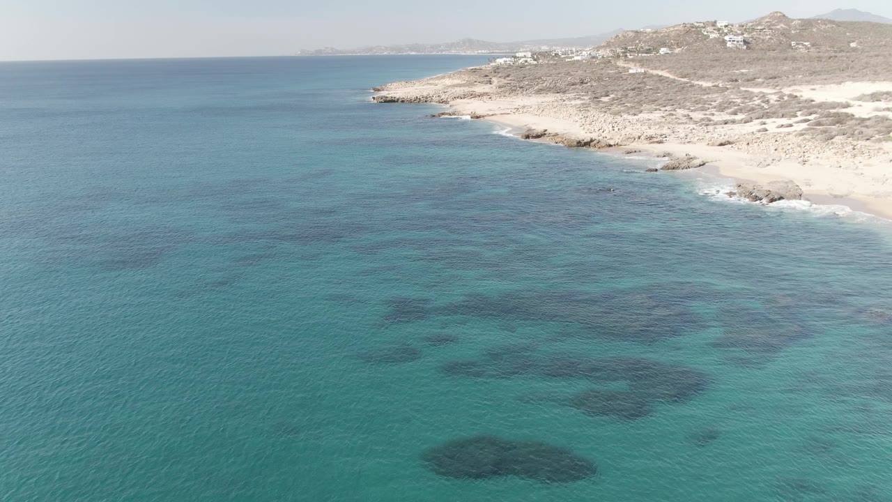Turquoise sea with dark reef patches and a rocky beach on the right.