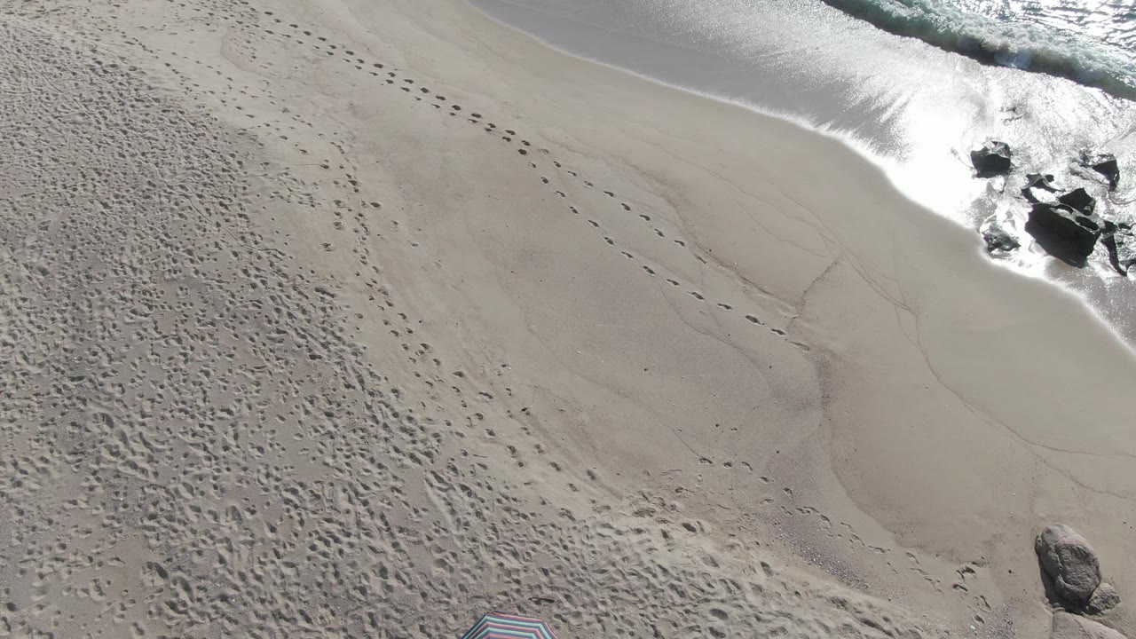 Aerial beach view with wet sand, footprints, waves, and rocks