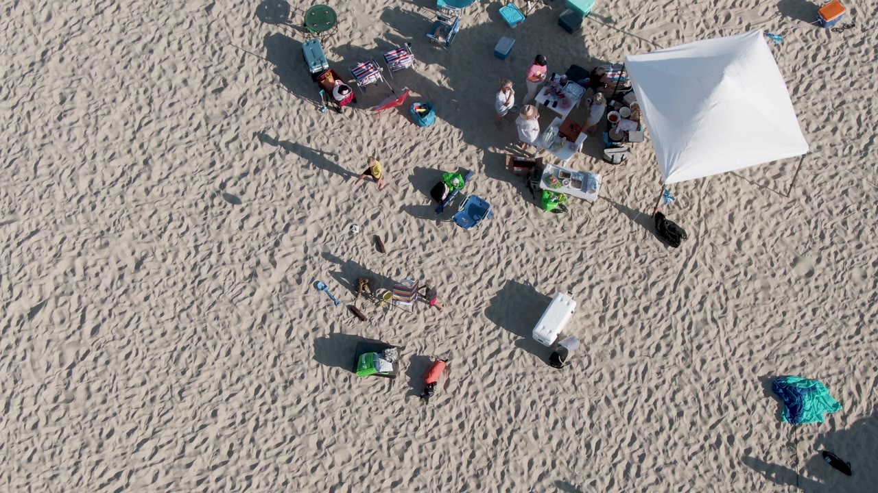 Beachgoers and gear clustered beside a white canopy.