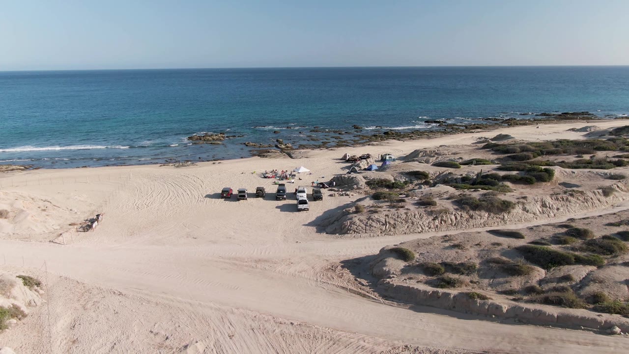 Vehicles and umbrellas on a wide sandy beach beside blue ocean water.