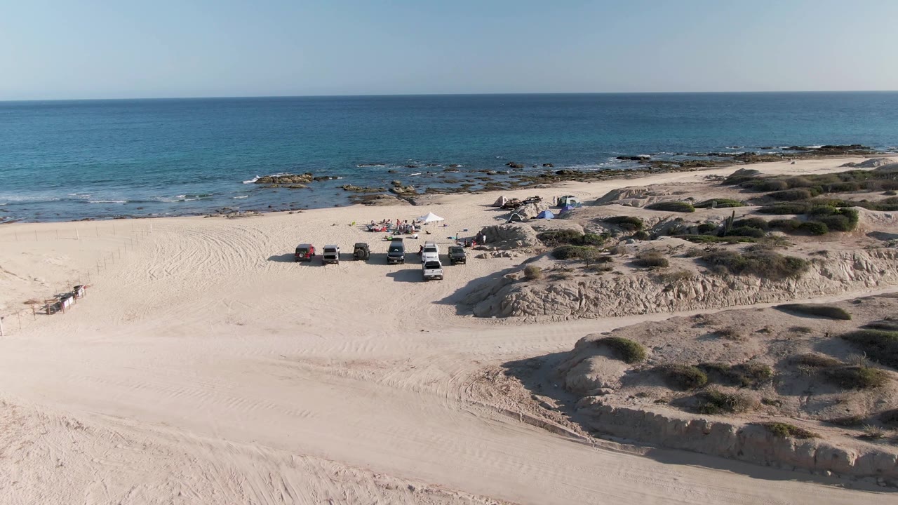 Vehicles and beach campsite seen from above beside blue ocean.