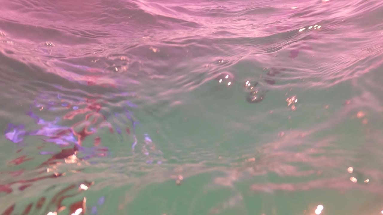 Close underwater view in San Jose Del Cabo, Mexico with the water surface filling the upper frame, pink reflection, green water below, and no visible people.
