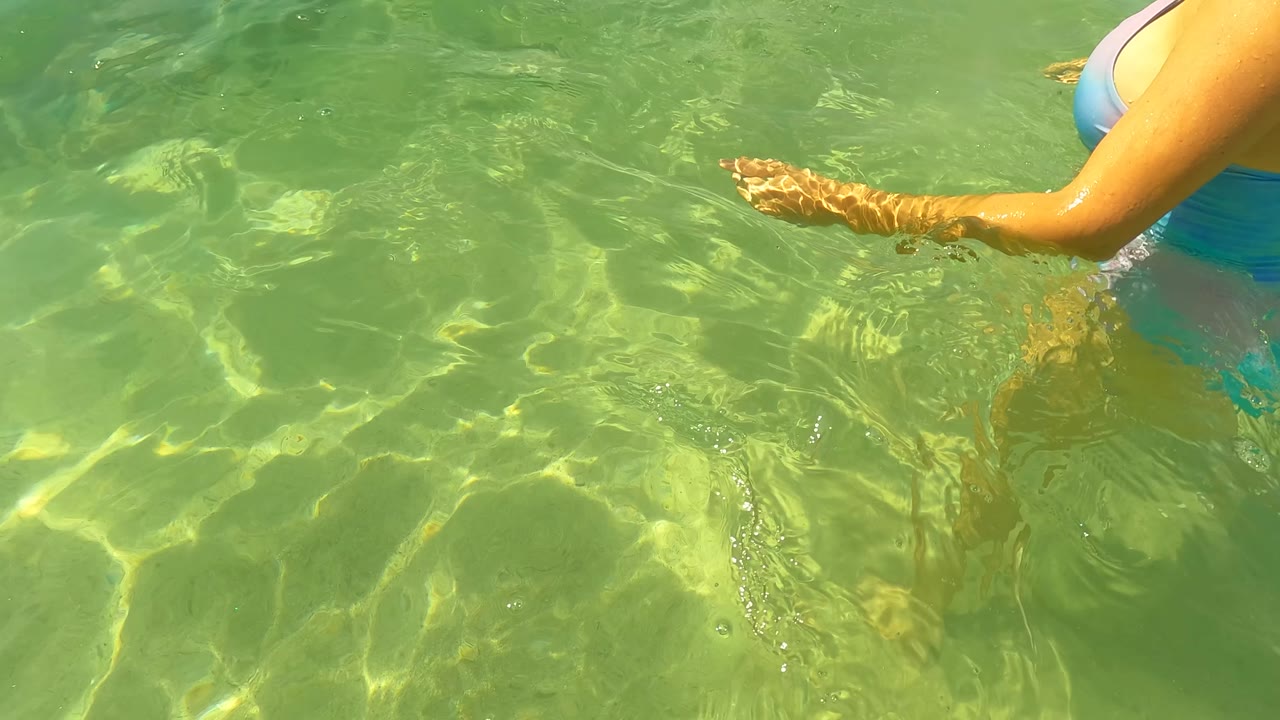 Woman's arm and swimsuit edge in clear shallow water