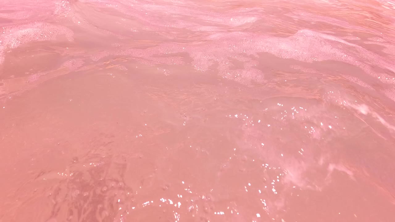 Pink-tinted surf water in San Jose del Cabo, Mexico, with white foam, small bubbles, and no visible people in the frame.