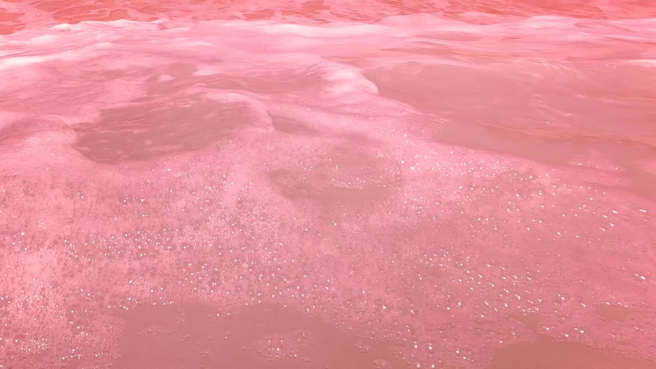 Foamy pink ocean water over shallow sand