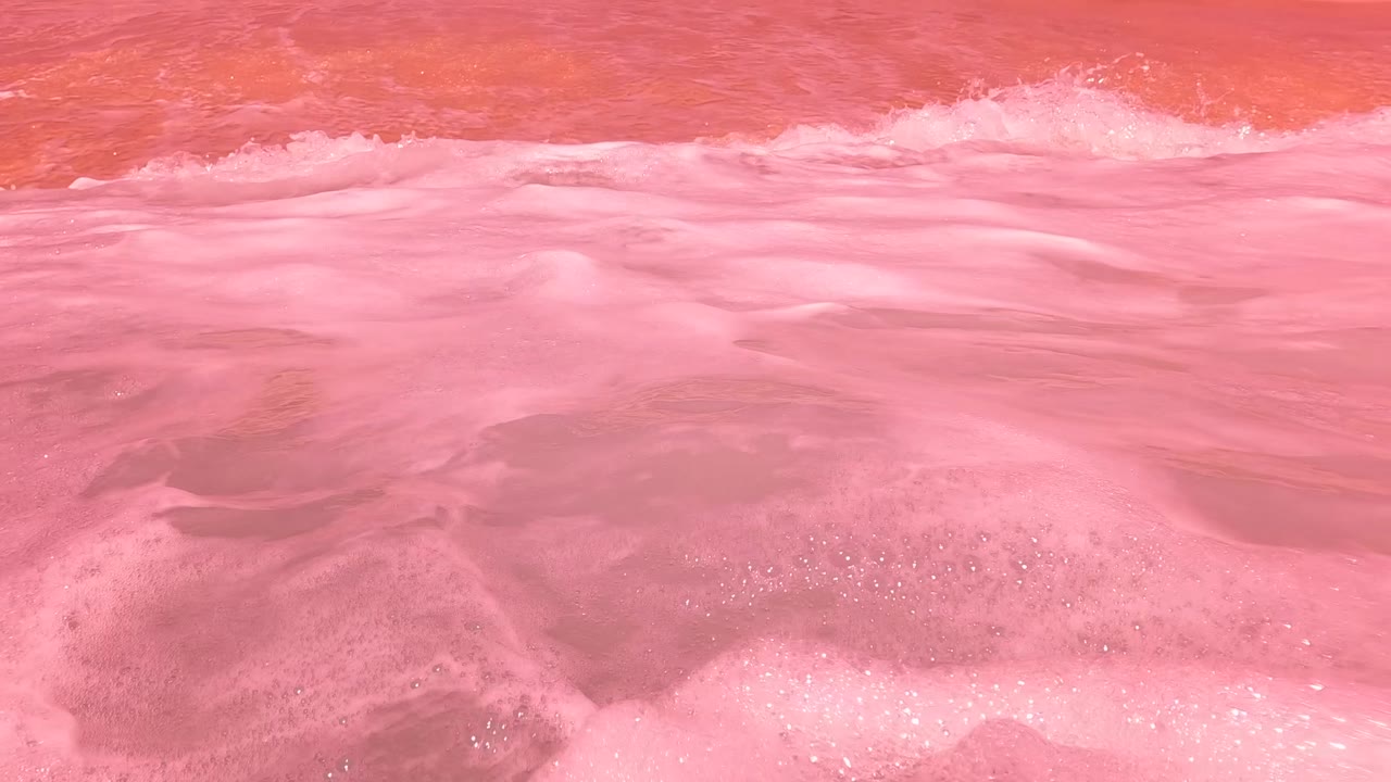A close water-level view of pink surf in San Jose del Cabo, Mexico, with white wash stretching across the frame and no visible people.