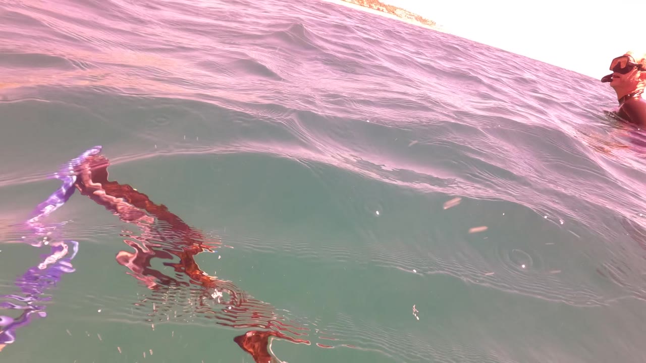 Waterline frame in San Jose Del Cabo BCS Mexico with rippled ocean surface, a small visible swimmer or body part near the edge, and pink light on the water.