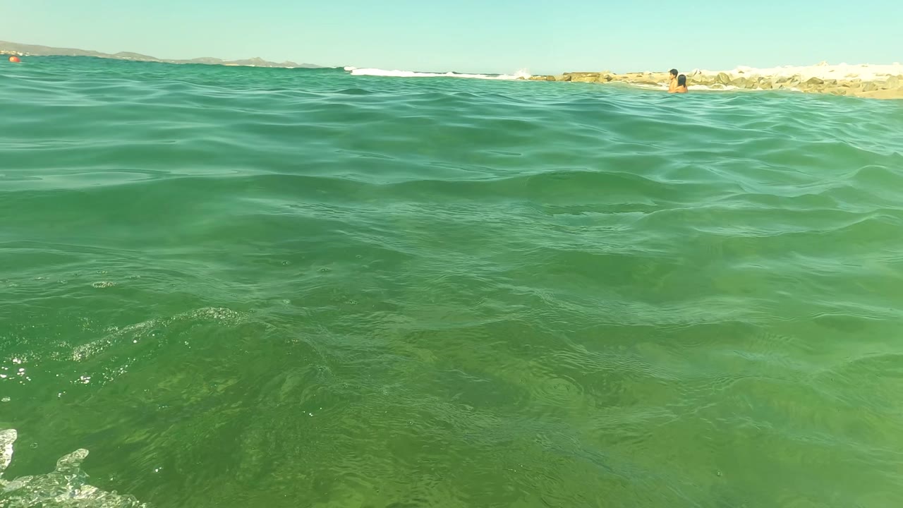Ocean surface near a rocky breakwater with tiny distant figures