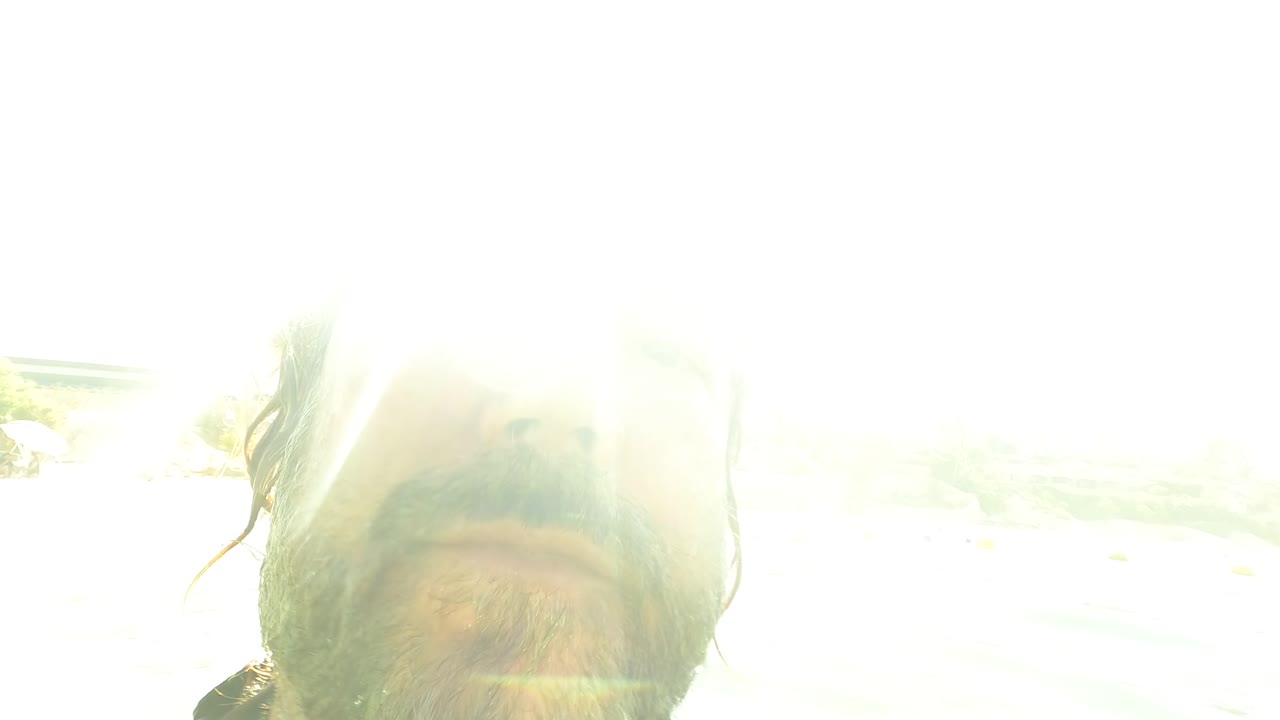 Overexposed frame from San Jose del Cabo, Mexico showing a close swimmer face partly visible below bright sun glare at the ocean surface.