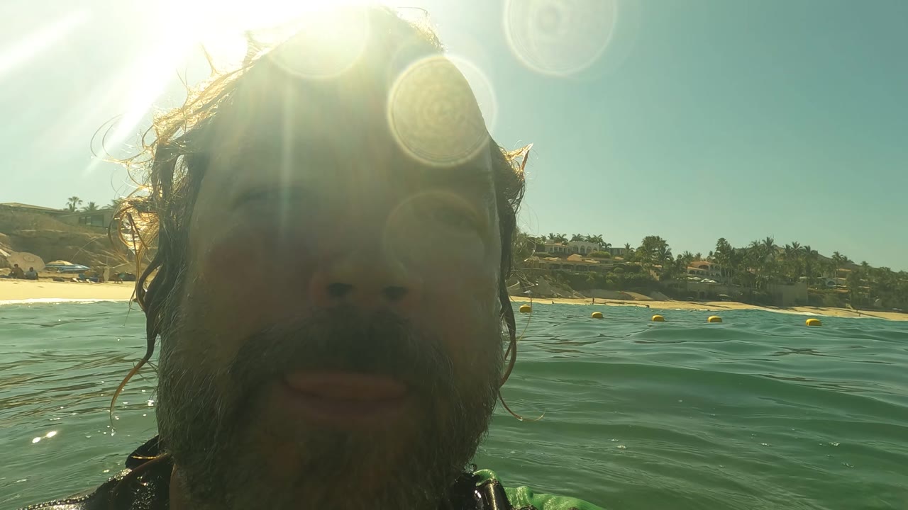 Close swimmer face at water level with beach in the background.