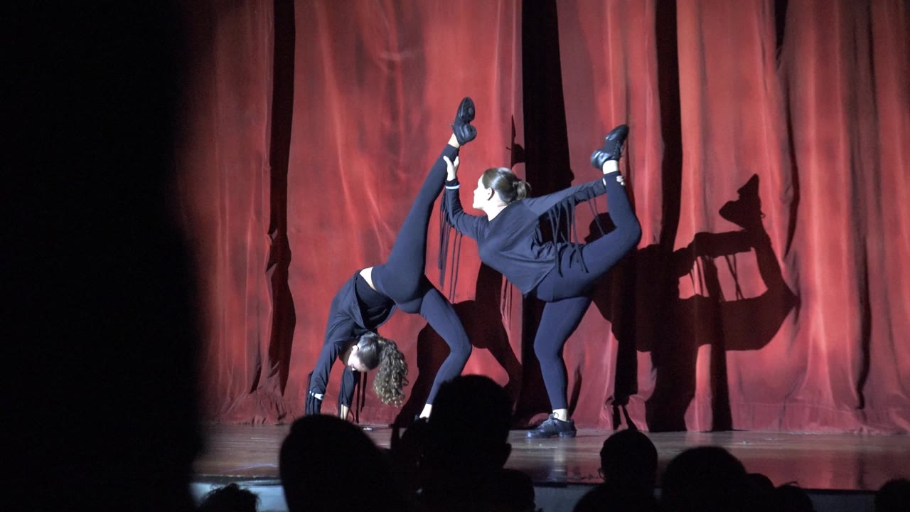 Two dancers maintain a synchronized pose under stage light.