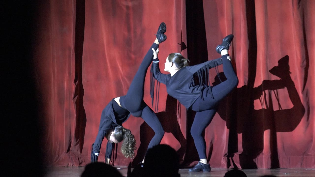 A closer moment in the sequence shows one dancer bent forward and the other extending a leg back, both lit sharply against the red curtain in San Jose del Cabo, Mexico.