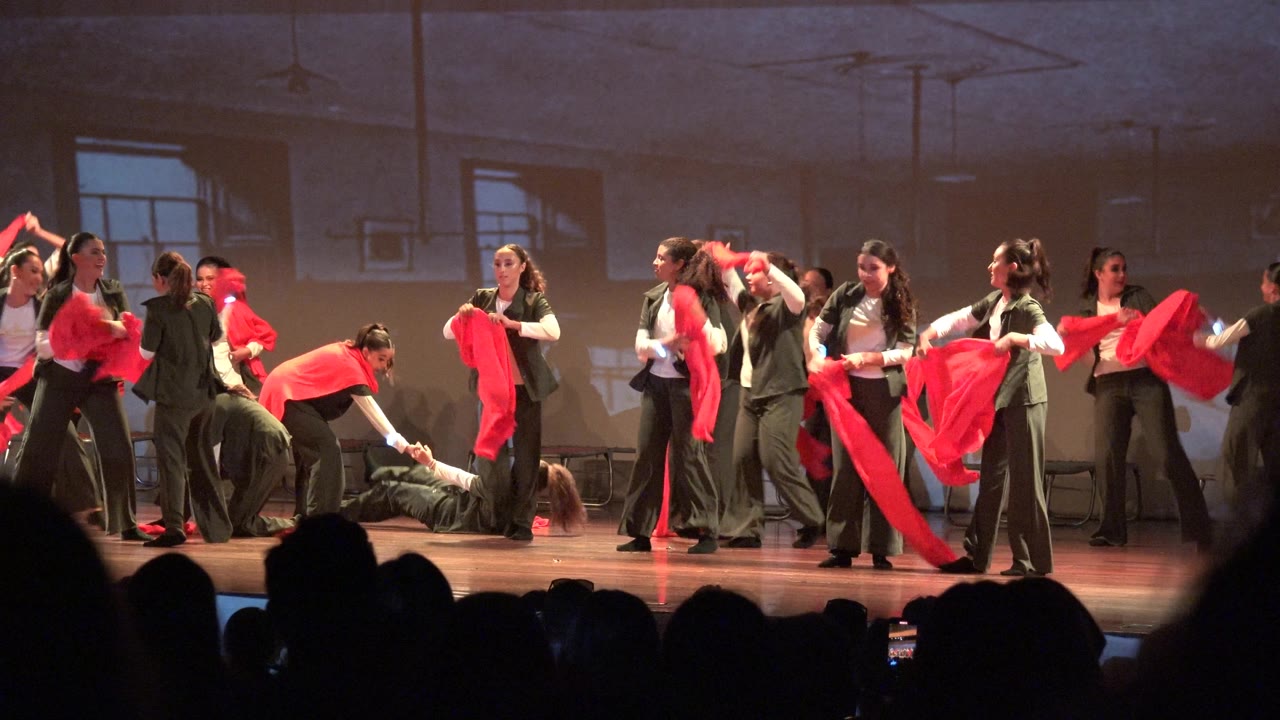 Dancers lift and sweep red scarves across a wide stage.