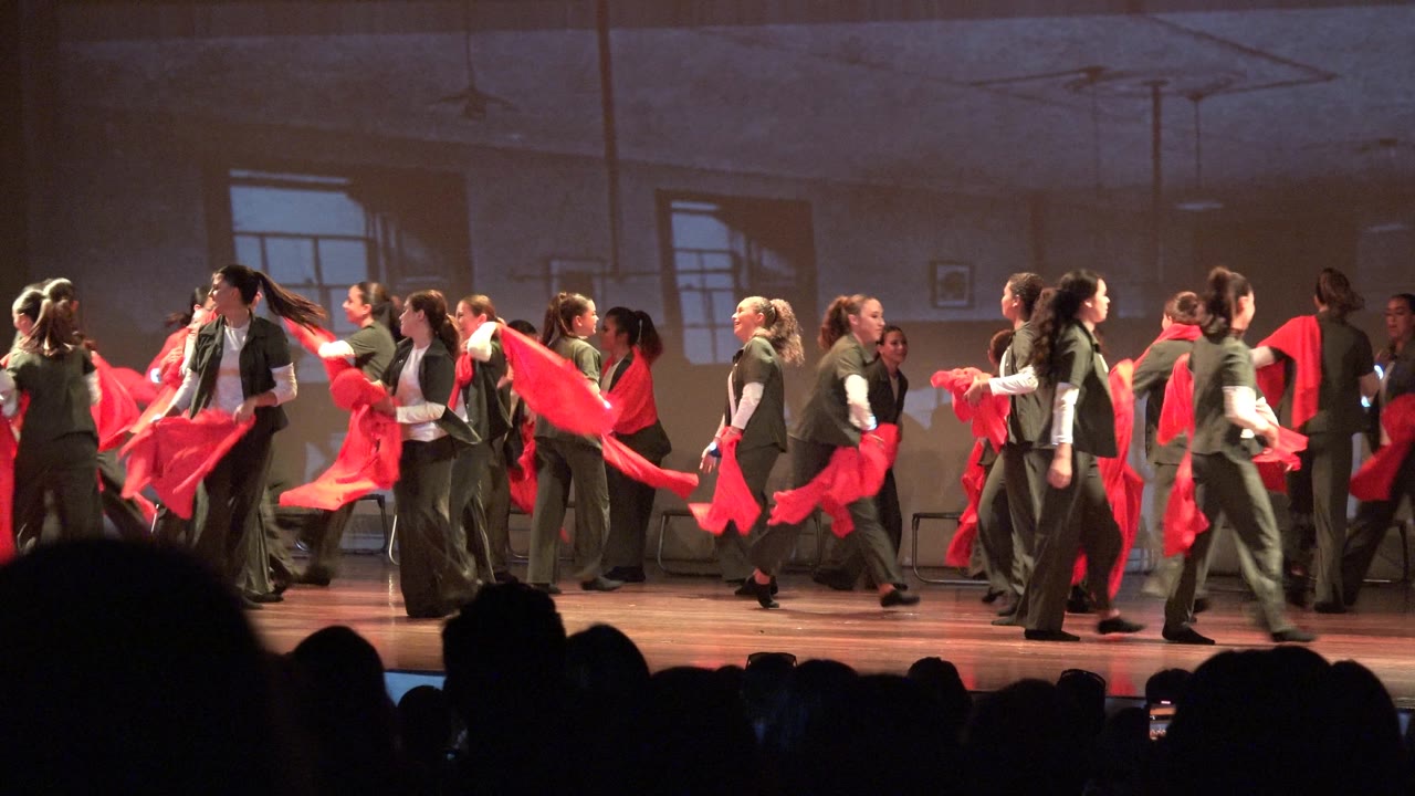 Stage dancers crossing paths while waving red scarves.