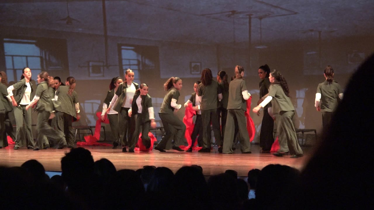 At 0:02 in San Jose Del Cabo BCS Mexico, the ensemble remains spread across the stage as dancers turn and pass one another with red fabric visible at both sides.