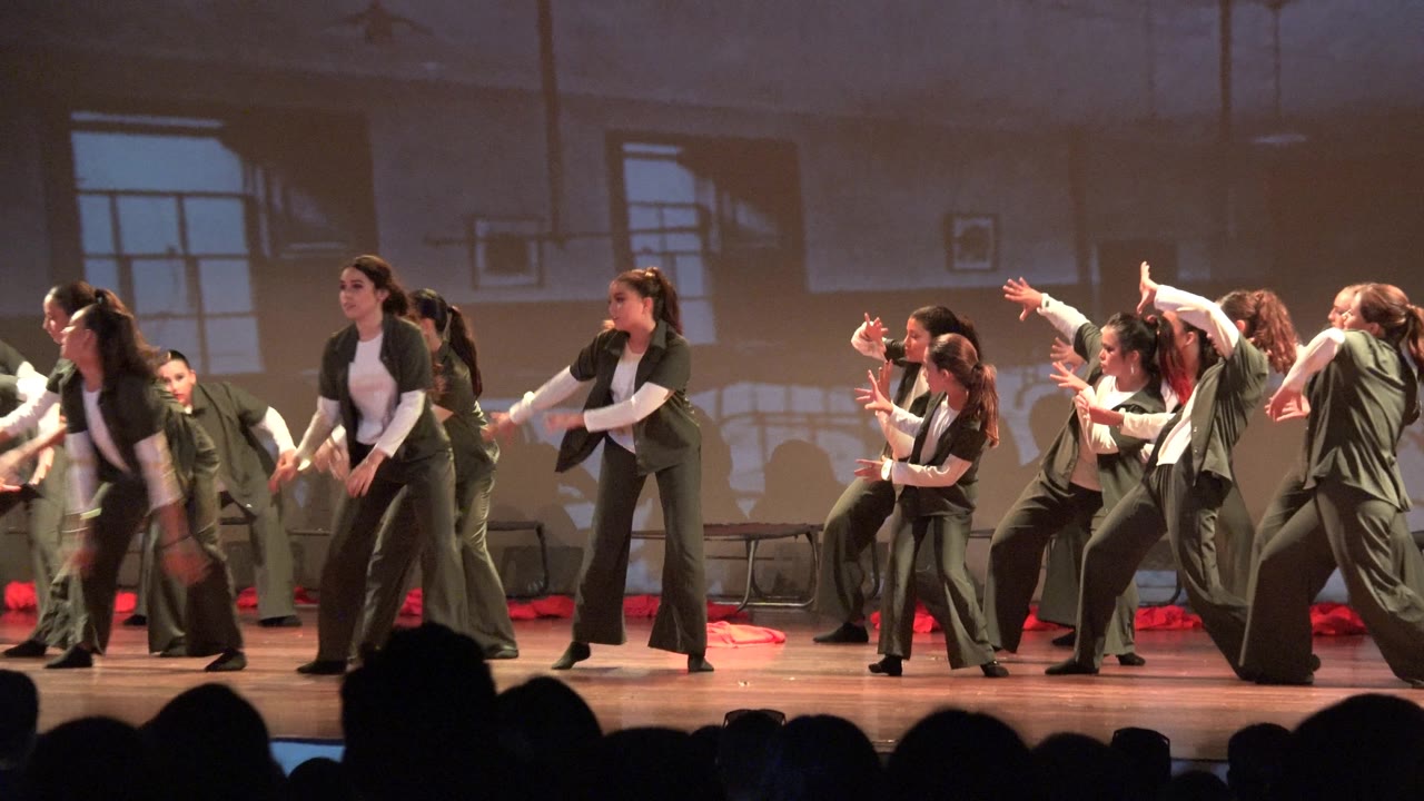 Group of dancers raise arms and shift positions on stage.