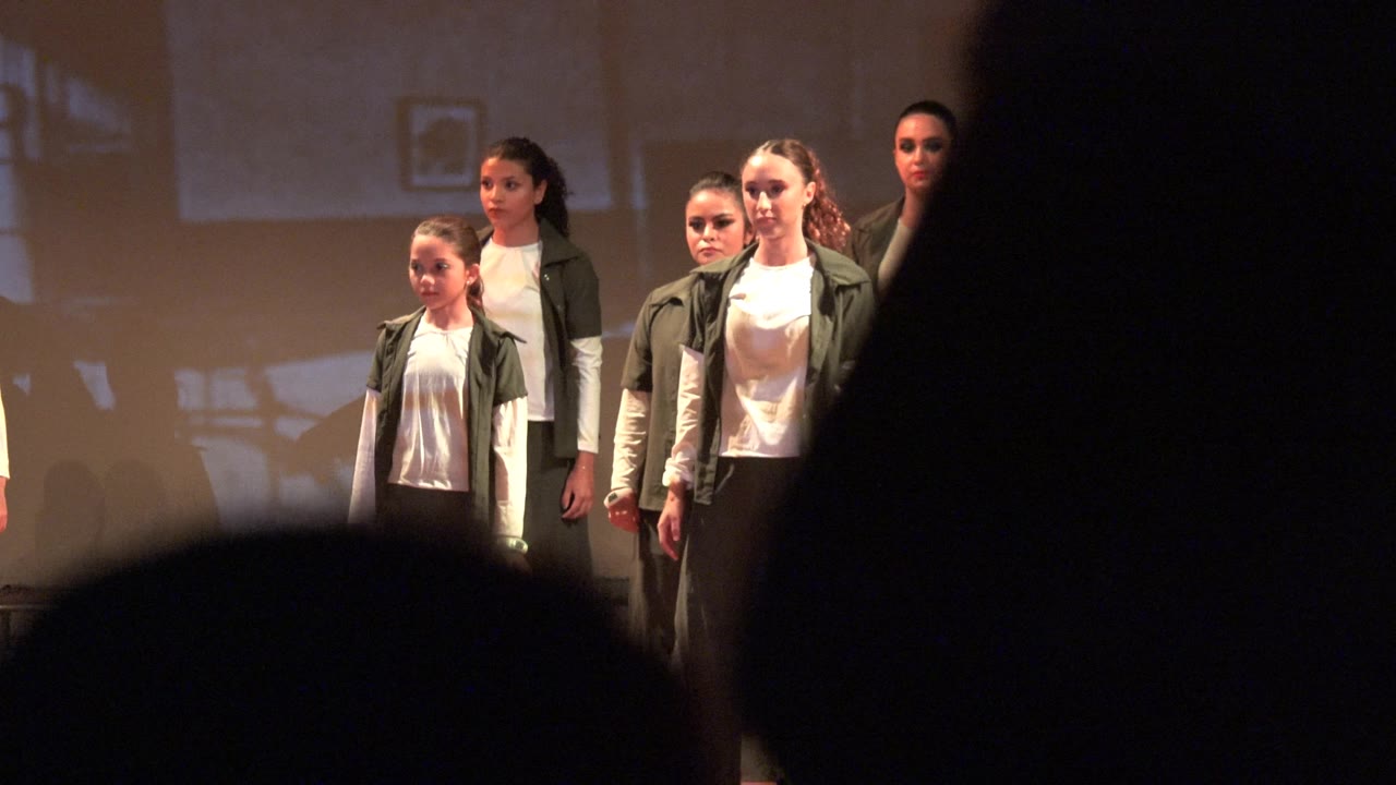 The dancers remain in a stage formation in San Jose Del Cabo BCS Mexico, but a large dark audience silhouette blocks much of the center and right side of the frame.