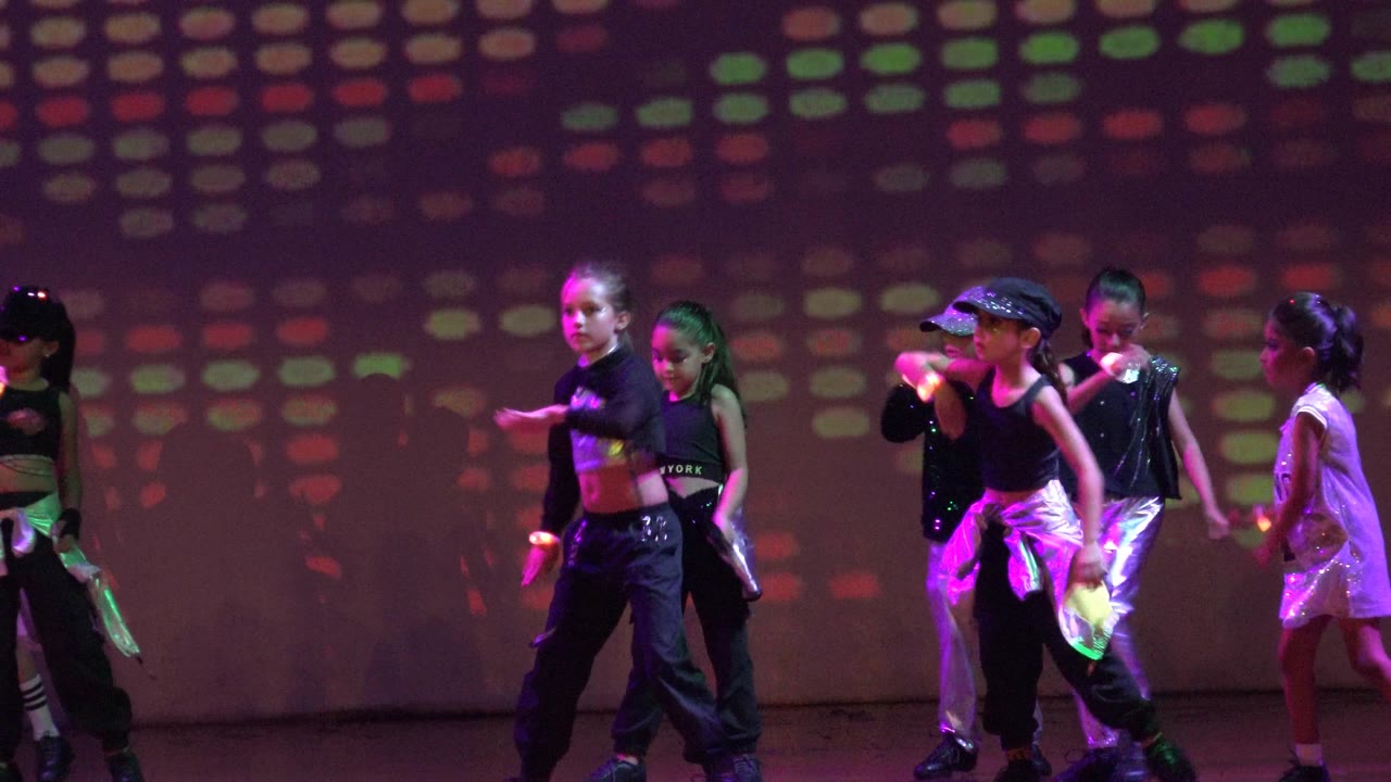 Young dancers in black and silver costumes cross the stage.