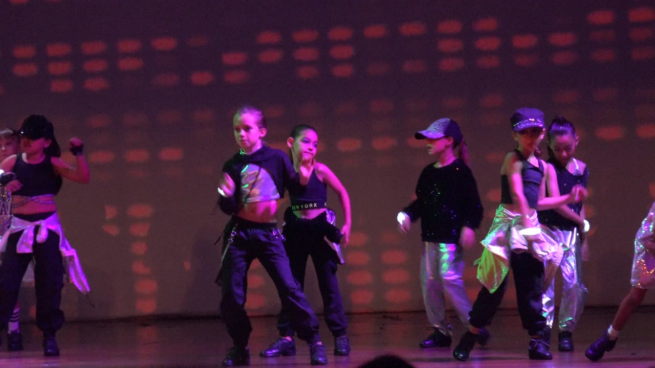 A cluster of children dances near center stage in San Jose del Cabo BCS Mexico, with caps, black tops, shiny silver garments, and dotted colored lights behind them.