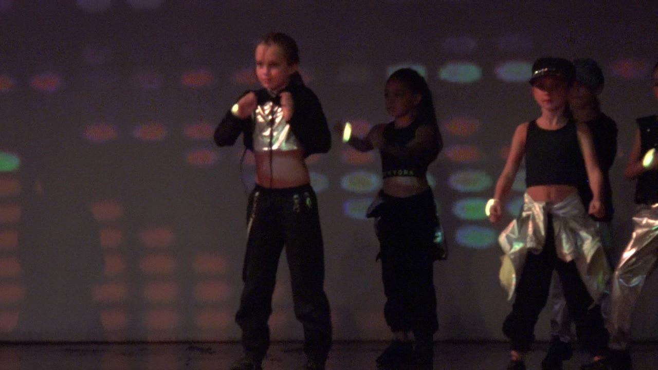 Dancers in dark outfits stand and move on a San Jose Del Cabo BCS Mexico stage with glowing wristbands and soft colored projections behind them.