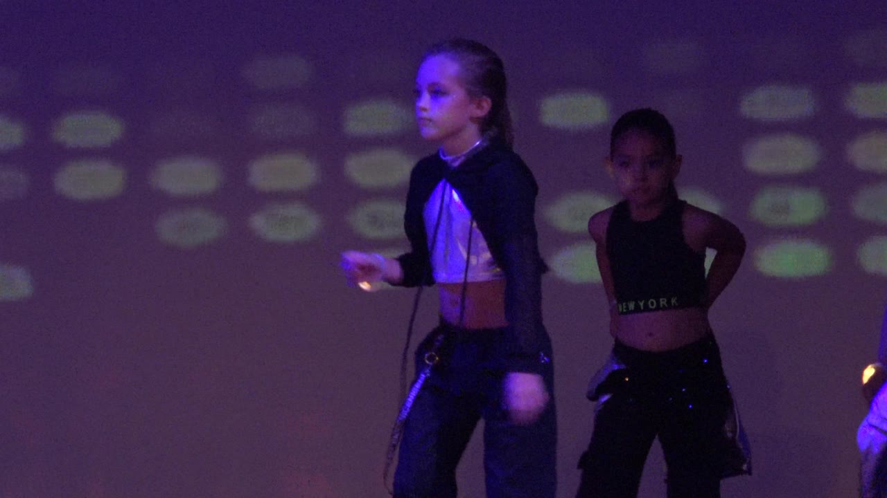 Children perform on a stage in San Jose Del Cabo BCS Mexico, with a girl in a black and silver outfit foregrounded and colored light spots on the backdrop.