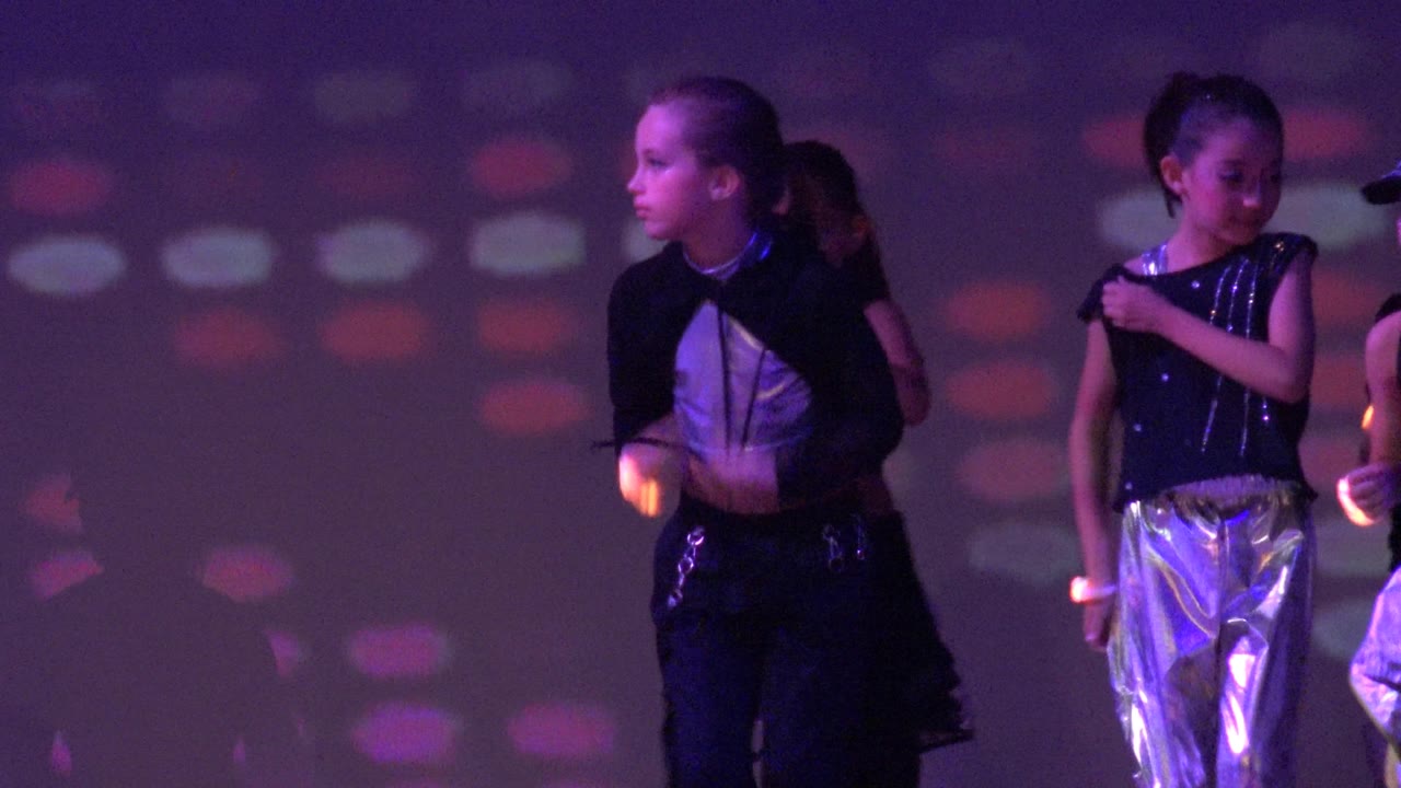 Children in shiny costumes moving across a lit stage