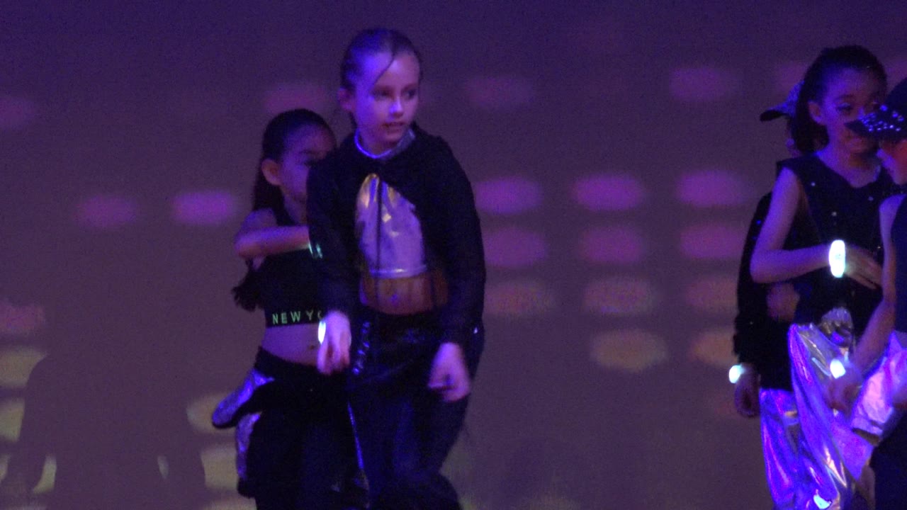 Two children cross near center stage in San Jose Del Cabo BCS Mexico, with other young performers partly visible against purple and red projected lighting.