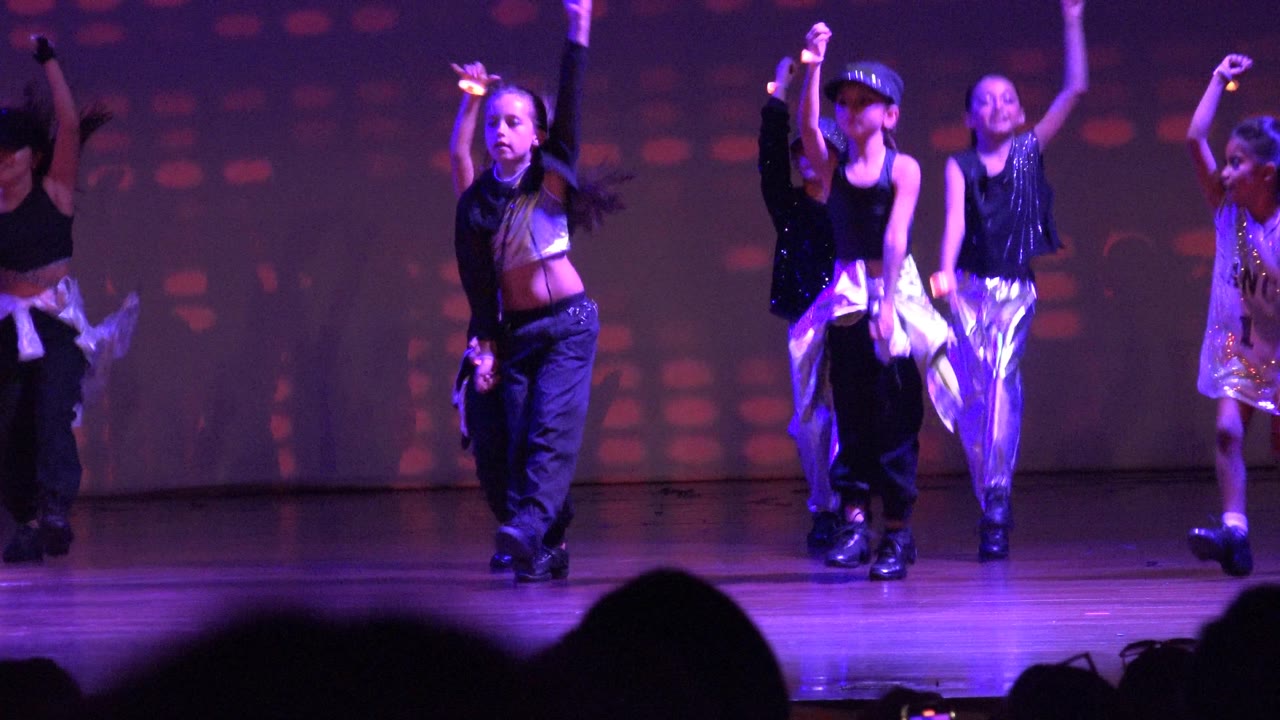 Children remain spread across the San Jose del Cabo, Mexico stage as the front dancers step forward and the projected backdrop shows soft colored dot patterns.