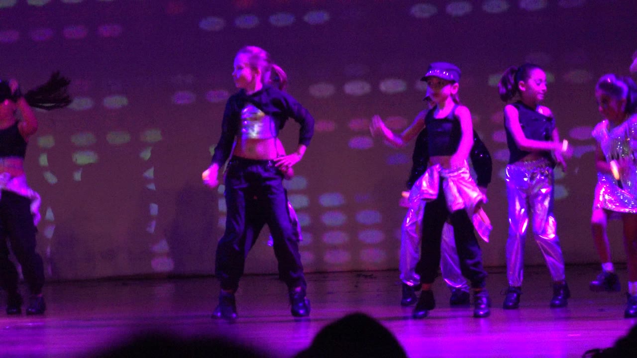 Young dancers perform on a purple-lit stage in San Jose Del Cabo BCS Mexico, with black outfits, shiny silver clothing, and a dotted light projection across the backdrop.