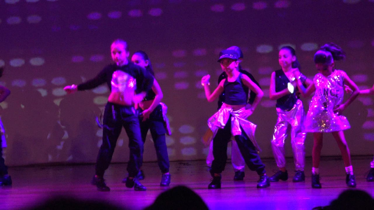 Youth dance group mid-routine under purple stage lights.