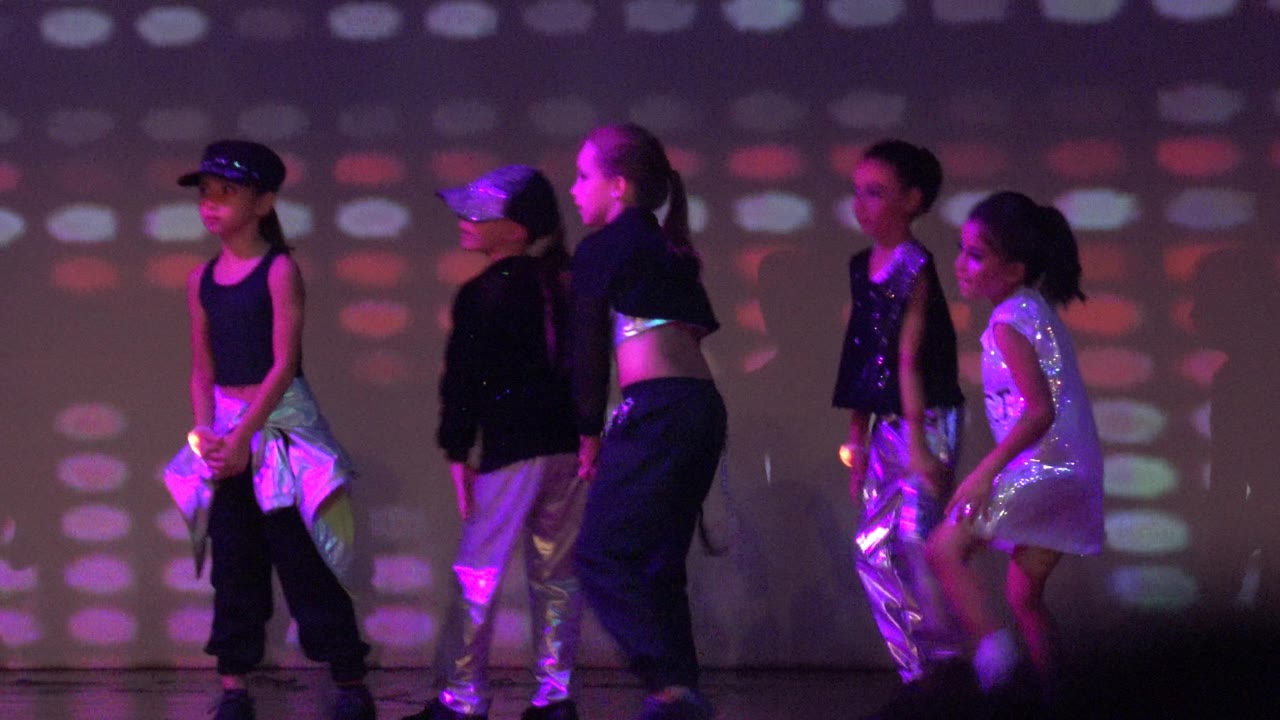 Children in black and silver outfits begin a stage dance routine in San Jose Del Cabo BCS Mexico, with purple and red projected light patterns behind them.