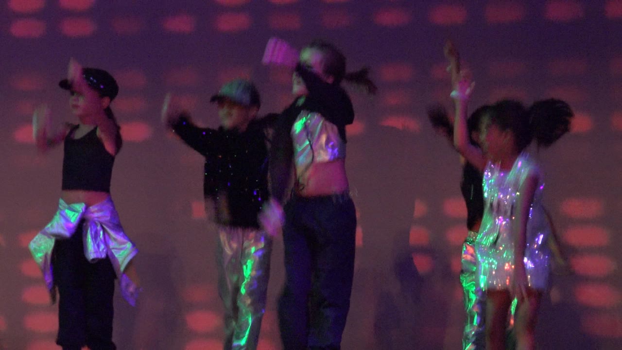 Children continue a synchronized stage dance with arms raised.