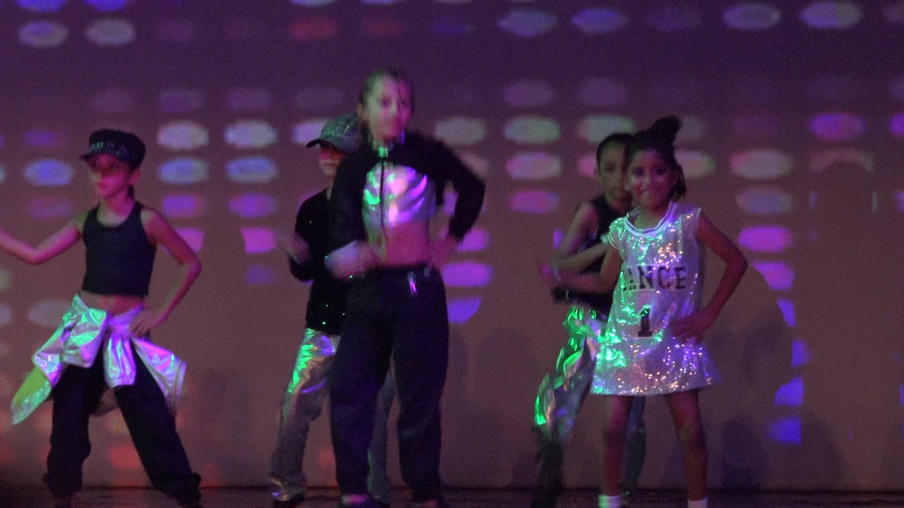 Children pose and step in formation on a lit stage.