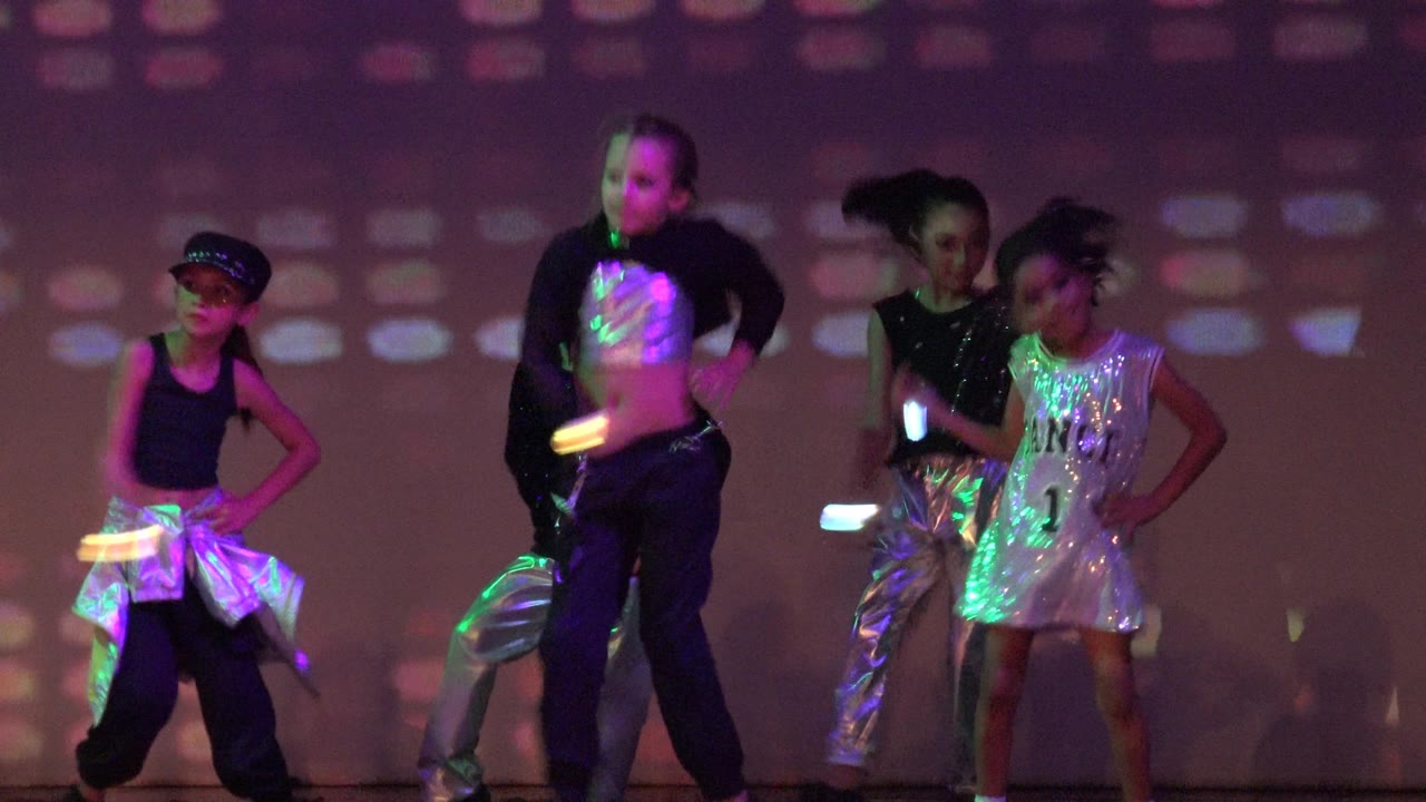 Children in shiny costumes pose during a dance routine.