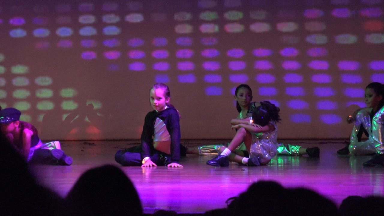 Seated child performers onstage with multicolored light blocks behind them.