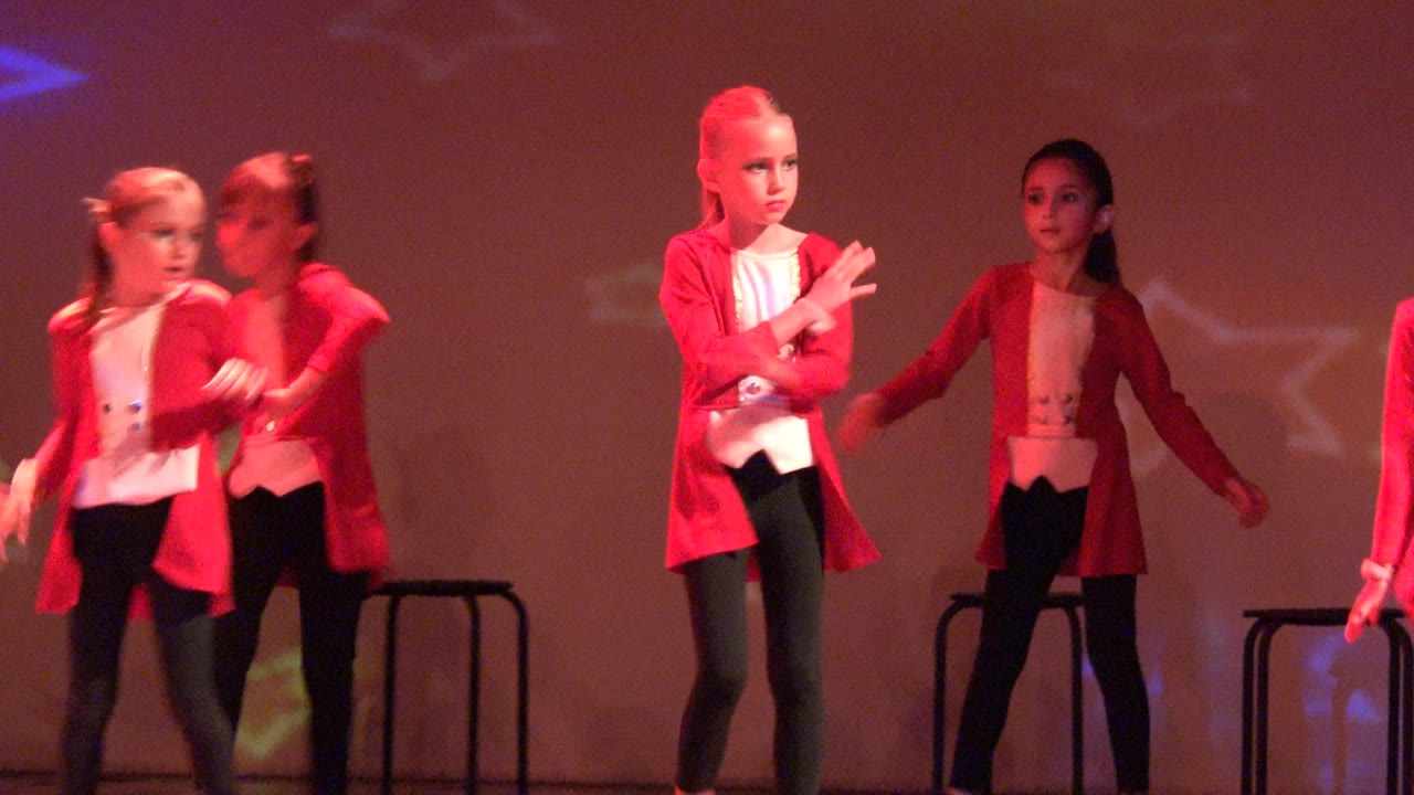 At 0:00, children in red jackets and black pants perform on a stage in San Jose Del Cabo, Mexico, with dark stools behind them and colored projection light on the backdrop.
