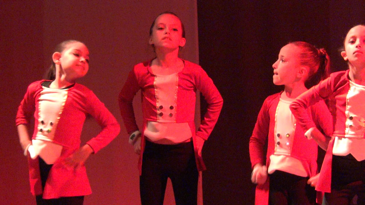 Two young girls in red tops hold dance poses on stage.