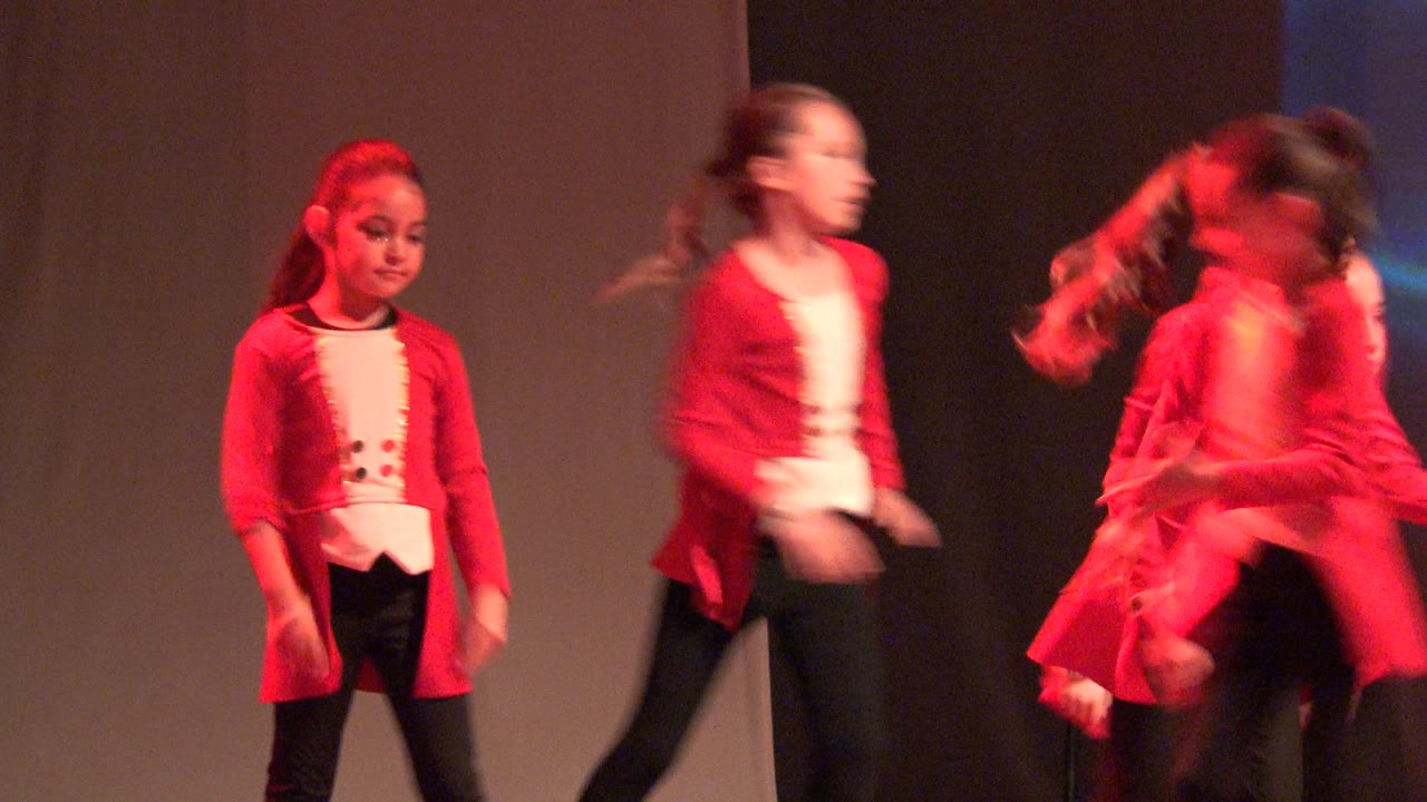 A group of young girls in red and white costume tops move through choreography on a red-lit stage in San Jose Del Cabo BCS Mexico, with some motion blur from the dance.