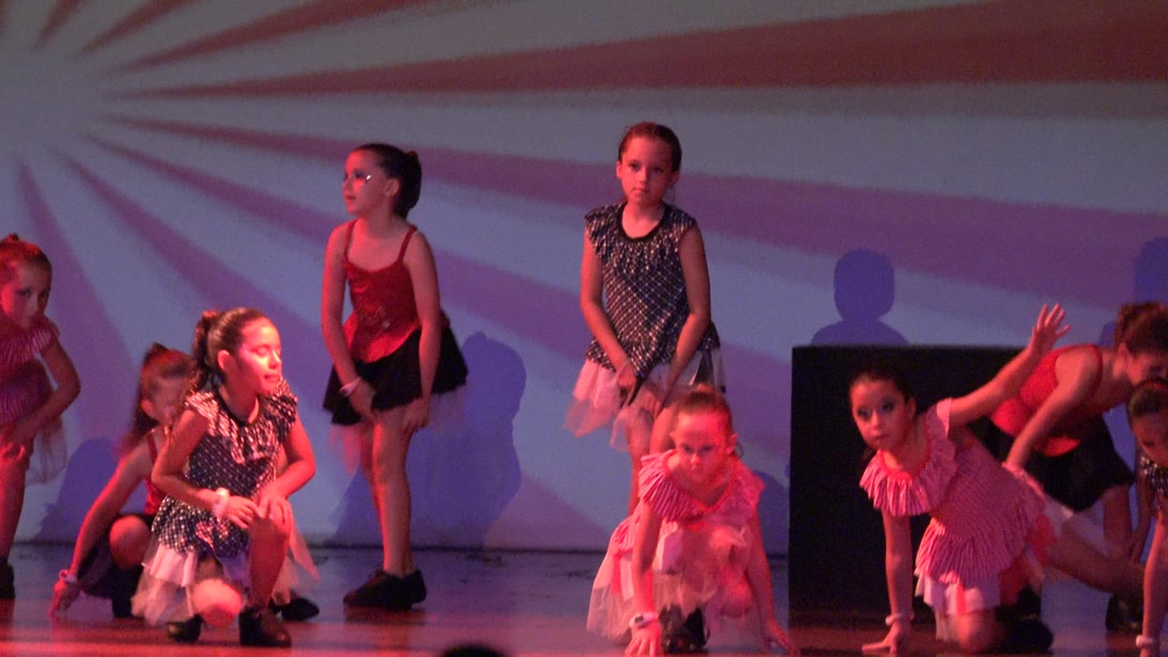 Girls in dance costumes kneel and stand on stage.