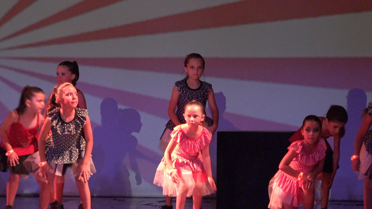 Young dancers continue the routine in San Jose del Cabo BCS Mexico, with one child crouched near center and others reaching or leaning beneath red and purple stage wash.