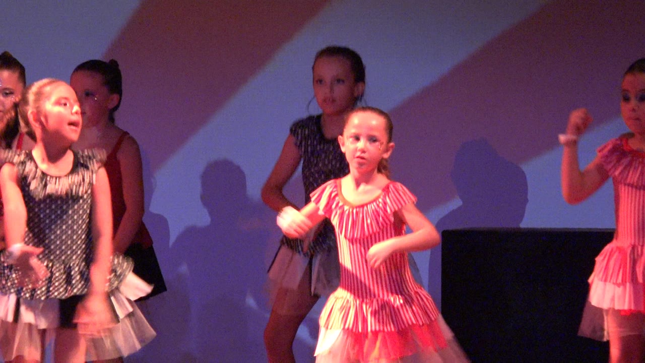 Young girls perform a synchronized dance routine on a stage in San Jose Del Cabo BCS Mexico, with pink striped costumes, dark polka dot costumes, and shadows cast on the backdrop.