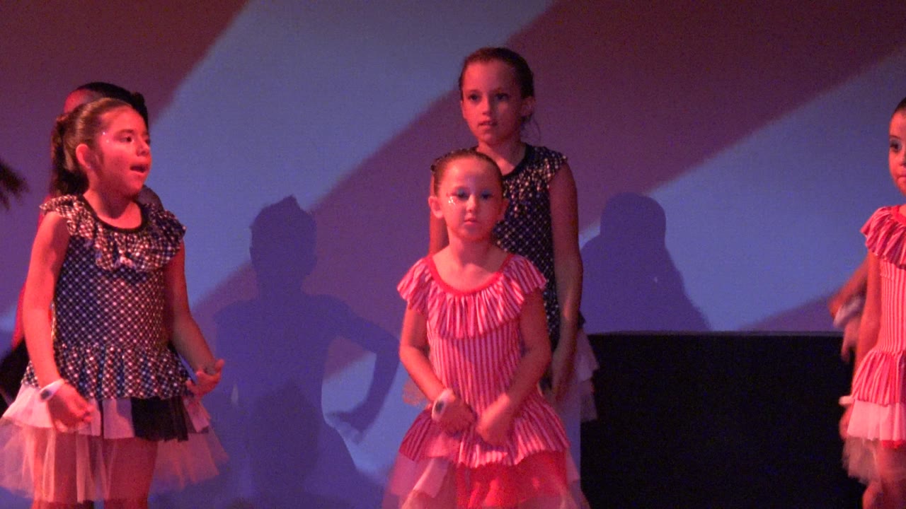 Children in matching dance outfits continue the routine in San Jose Del Cabo BCS Mexico, with one girl in a pink striped dress forward and other dancers behind her in darker costumes.