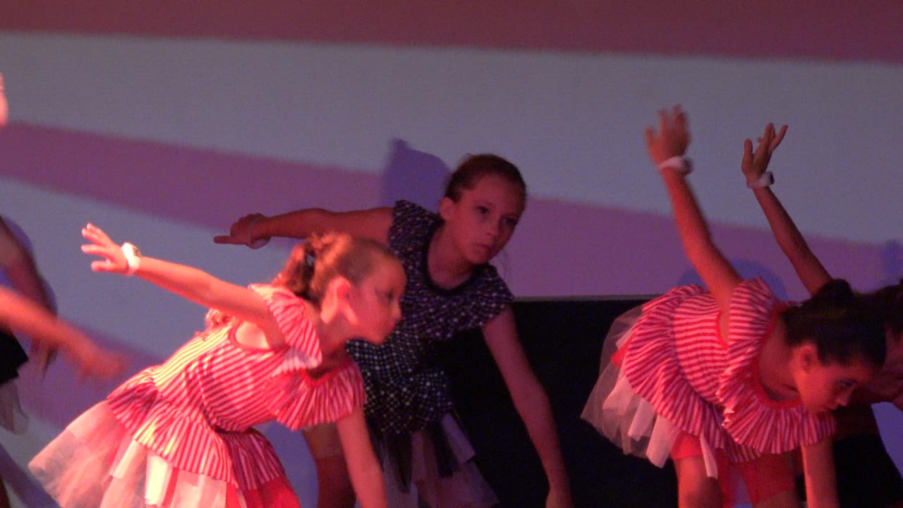 Young girls perform a stage dance in San Jose Del Cabo BCS Mexico, with one child leaning forward in a pink striped dress and another in a dark polka-dot costume behind her.