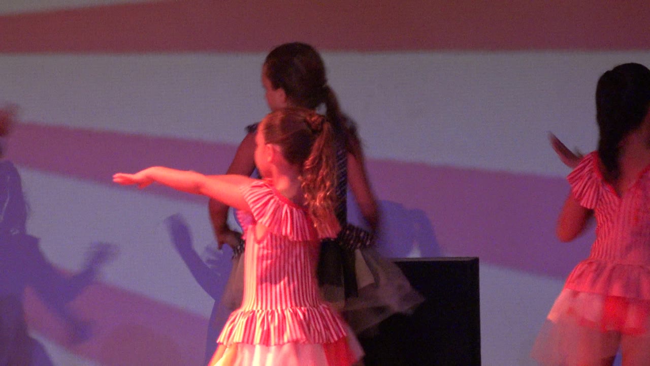 Girls in pink striped costumes dance on a stage in San Jose Del Cabo BCS Mexico, with one child pointing to the side and another turning near the striped backdrop.