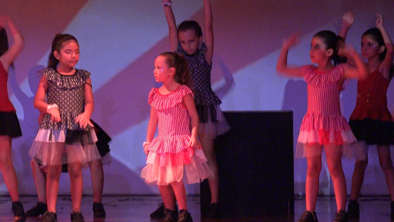 Young girls in polka dot and pink tulle costumes stand at the start of a stage dance in San Jose Del Cabo BCS Mexico, with purple and red lighting on the backdrop.