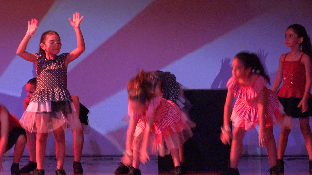 Girls raise their arms during a synchronized stage routine.