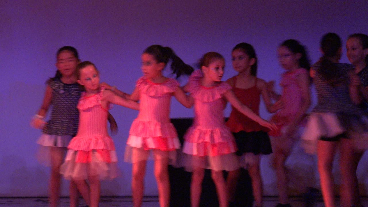 Young girls perform on a purple-lit stage in San Jose del Cabo BCS Mexico, with pink dresses, polka dot costumes, black shoes, and motion blur at the start of the routine.