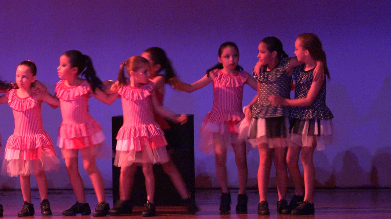 Girls holding hands in a line during a stage dance routine.
