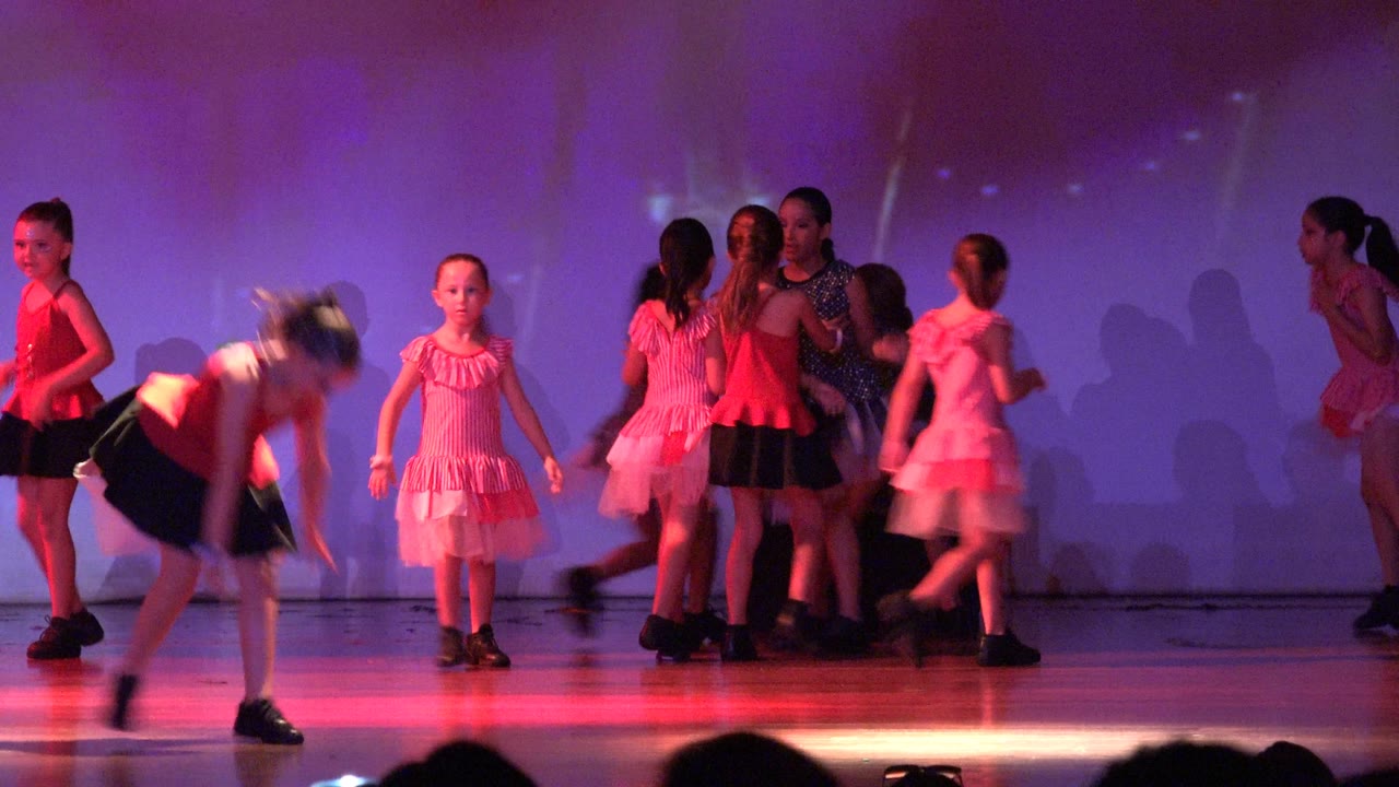A girl bends into a floor move while other dancers stand behind her.