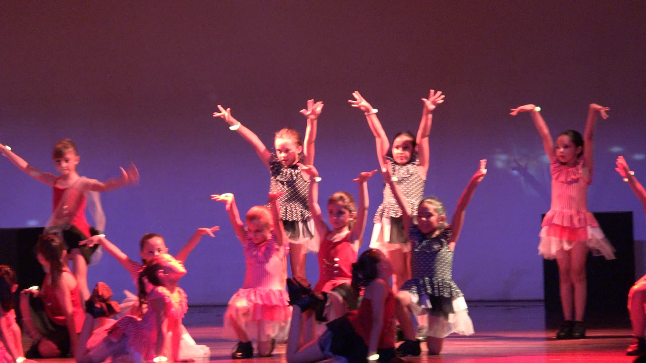 Young girls continue a synchronized dance routine on a purple-backed stage in San Jose del Cabo, Mexico, with one dancer centered and others kneeling or reaching upward.